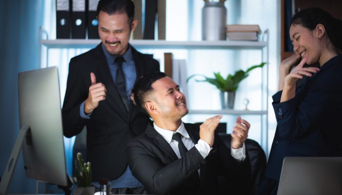 Three excited employees reading good news online in a computer sitting in a desktop at office